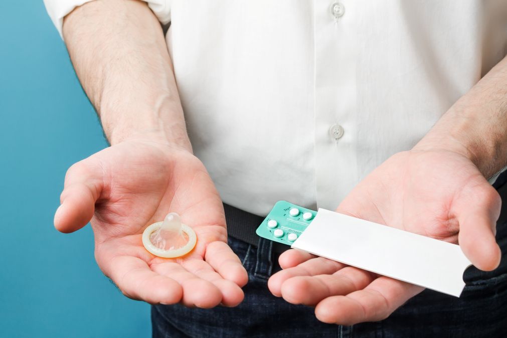 man holding condom and hormonal birth control pill pack